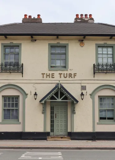 Un panneau montrant un visage souriant portant un bob, avec le texte "ALWAYS SUNNY WREXHAM TURF-TROPICANA"