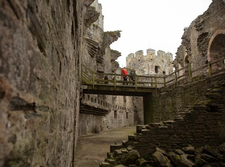 A couple of people standing on a wooden bridge in the middle of an old castle grounds