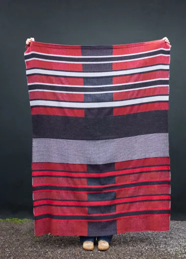 A person holding up a hand-woven red, white and blue striped blanket created by Welsh textile artist Llio James