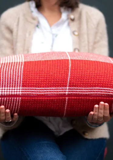 A person holding a red and white striped hand-woven cushion created by Welsh textile artist Llio James