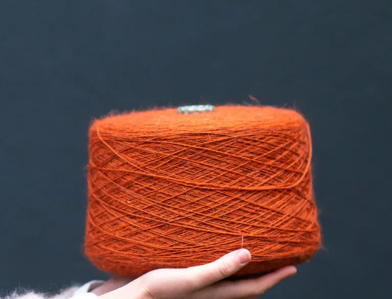 A hand holding a large reel of orange coloured wool