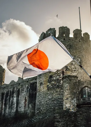 The Japanese flag being flown on a sunny day in front of the grand historic view of Conwy Castle in Wales, which is twinned with Himeji Castle in Japan