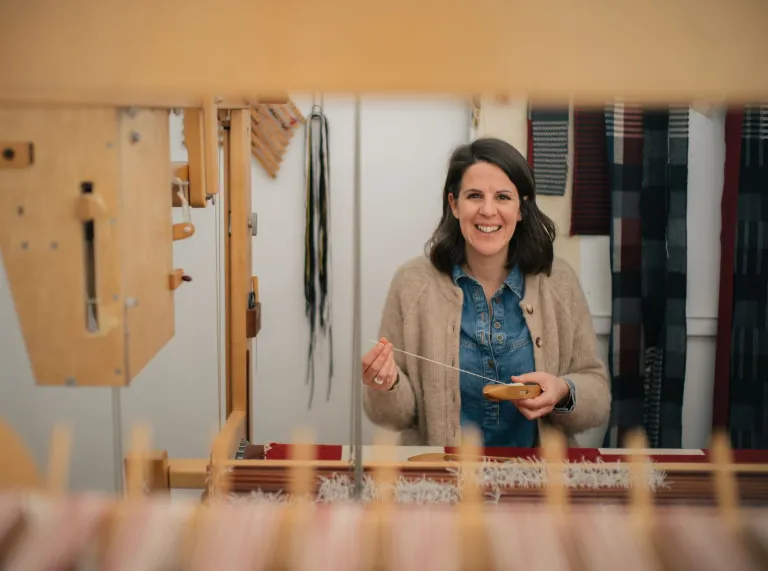 Welsh textile artist Llio James sitting at her hand weaving loom, smiling at the camera
