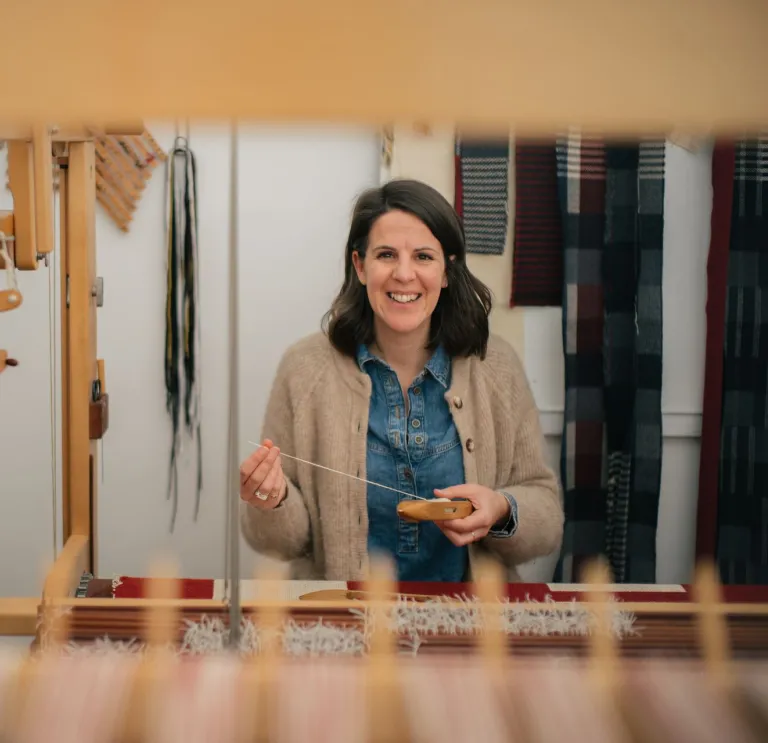 Welsh textile artist Llio James sitting at her hand weaving loom, smiling at the camera