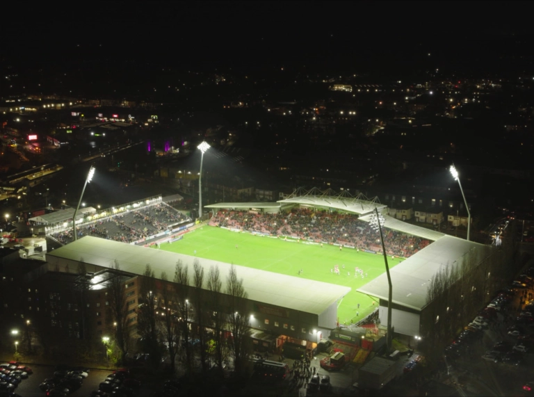 Aerial shot of Wrexham AFC football stadium at night, with lights shining on the pitch and a game being played