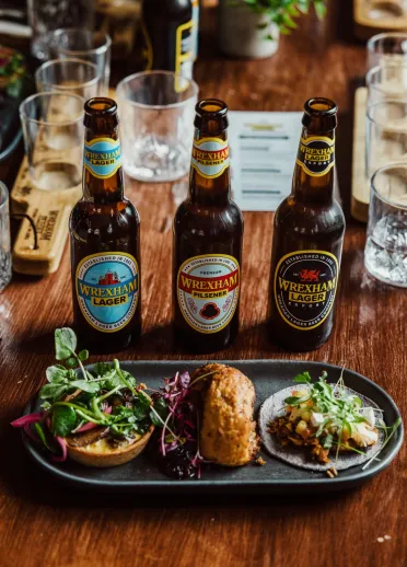 Picture of three bottles of Wrexham Lager beer paired with different appetisers on a pleasing grey plate