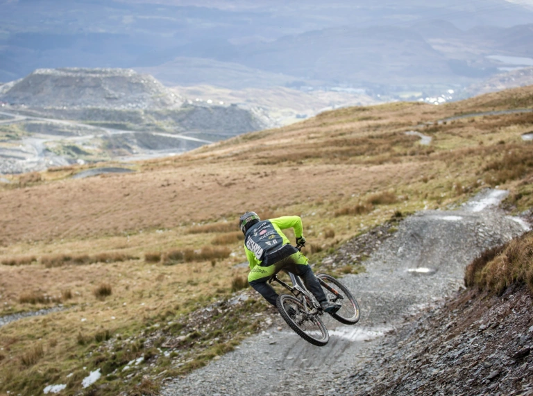A person on a mountain bike doing jumps on a mountainside downhill trail.