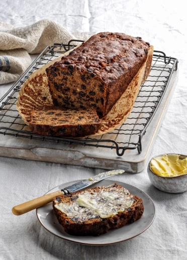 Ein Laib Bara Brith und eine Scheibe mit Butter darauf.