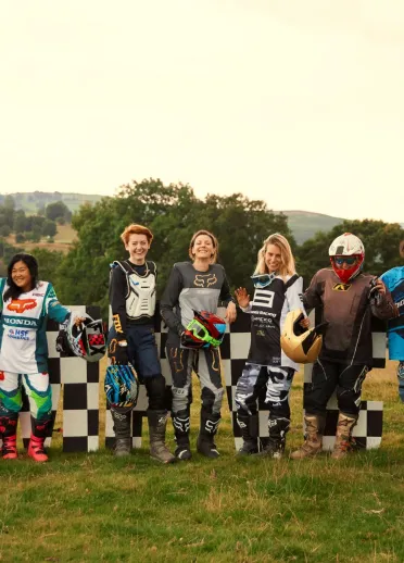 A group of womxn in motorbiking gear, standing in a line and smiling at the camera
