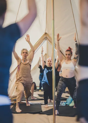 A group of womxn doing yoga in a festival tent