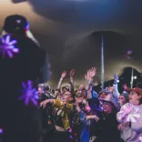 A crowd of people at a festival dancing and singing while looking up at a stage