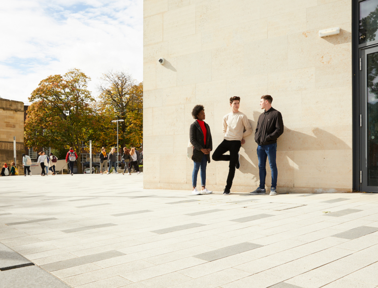 female and two males stood by building with people walking in background