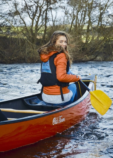 A young woman sitting in a canoe on a river.