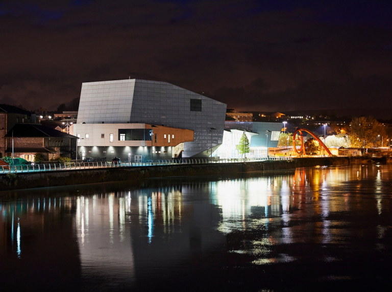 nighttime photo of riverfront, with lights from building reflecting into the river