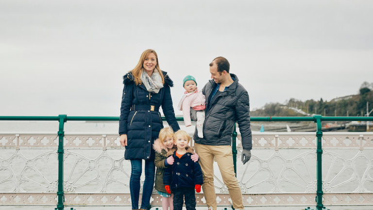 A man and a woman with their three children standing against the railing of a pier