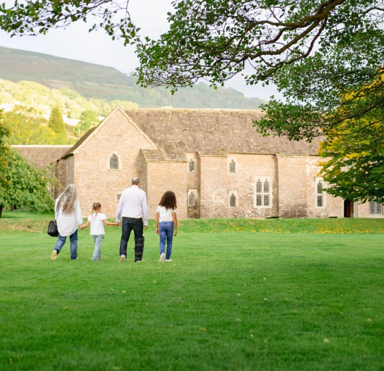 family in field walking towards a stone building.