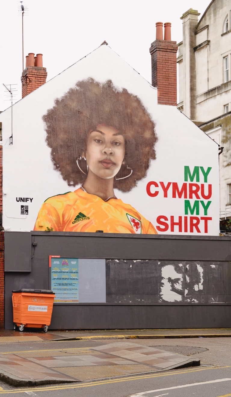 A huge mural of a woman wearing a yellow football shirt, on the side of a building.