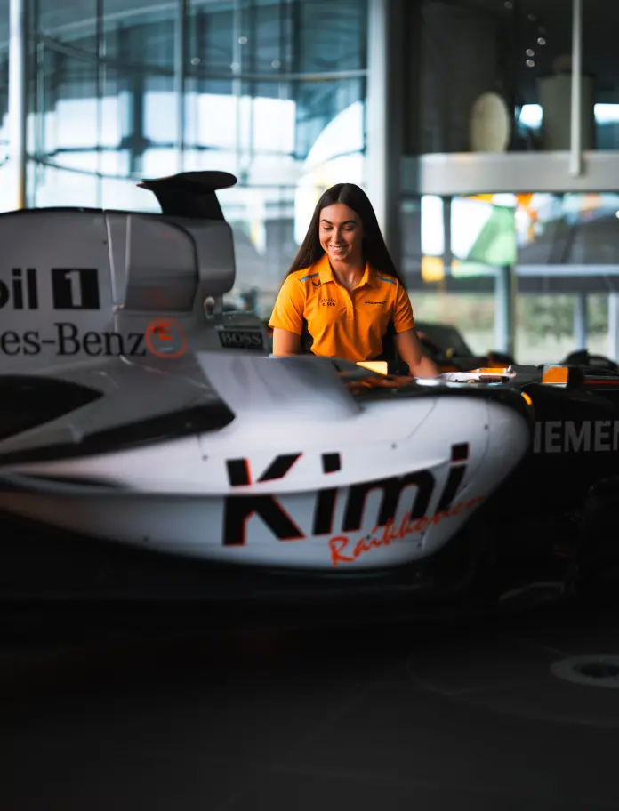 A close-up of driver Ella Lloyd posing with one of the McLaren racing cars.