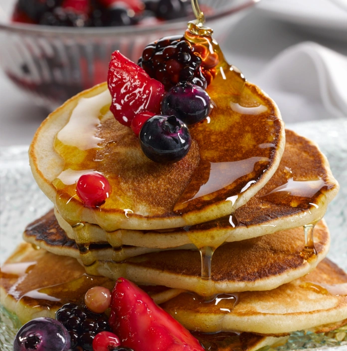 A pile of crempog (Welsh pancakes) with berries and syrup