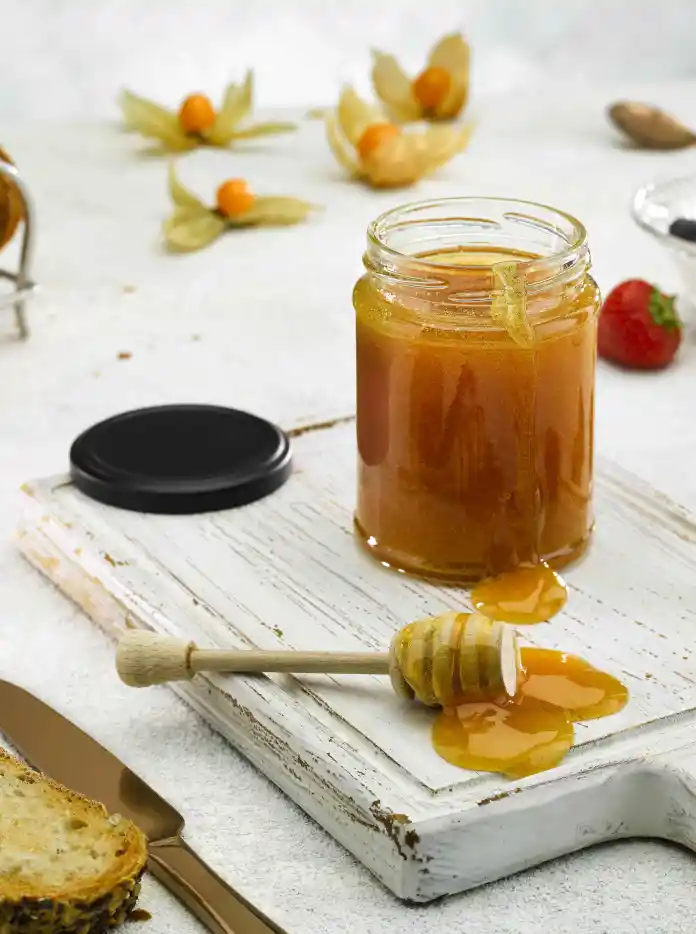 A pot of honey with toast and red berries.