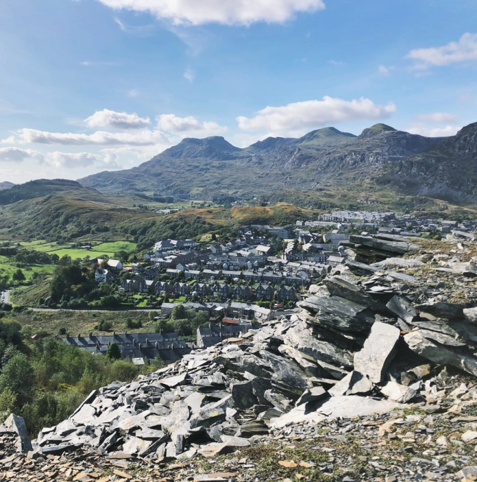 A mountain of slate in the foreground, with terraced houses and further mountains in the background
