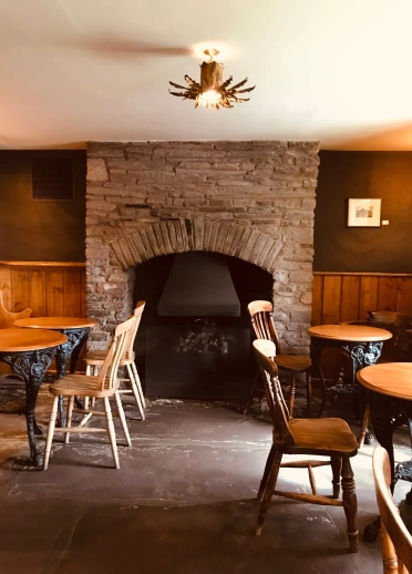 Einrichtung eines Restaurants mit Holztisch und Stühlen und einem großen Kamin im Hintergrund.