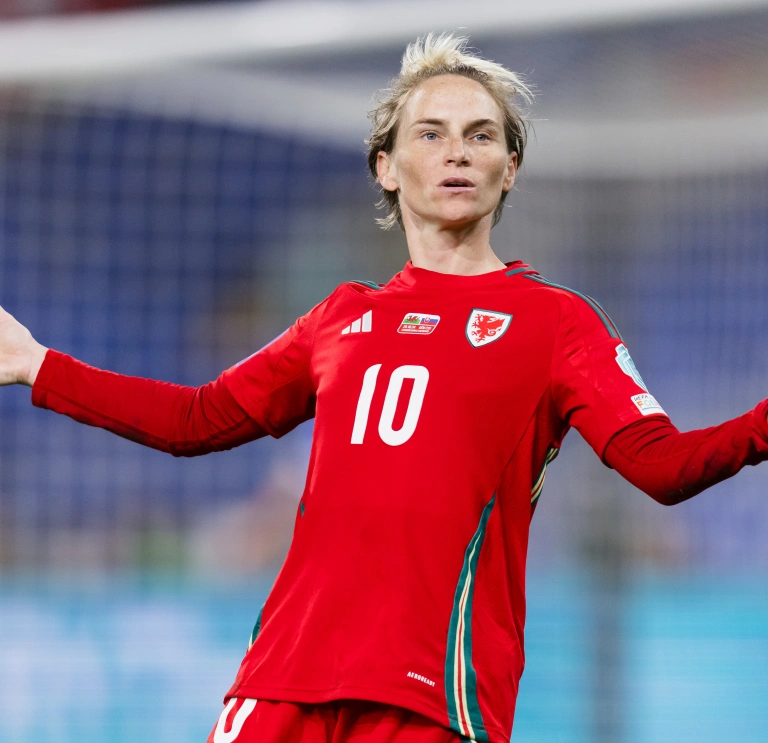 Dressed in her number 10 red football jersey, Fishlock stands with her arms out to her sides with a questioning look on her face 
