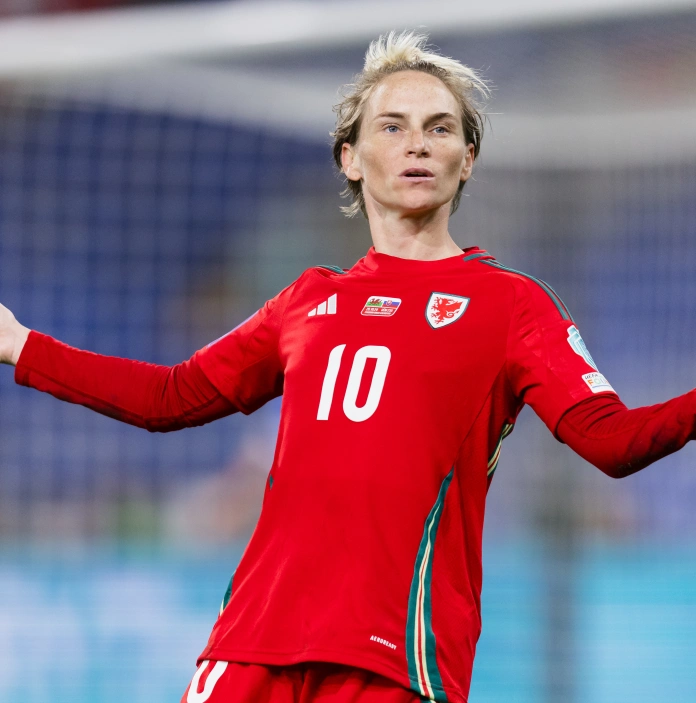 Dressed in her number 10 red football jersey, Fishlock stands with her arms out to her sides with a questioning look on her face 
