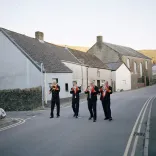 Four members of a traditional Welsh brass band playing their instruments, walking along a typical Welsh valleys street
