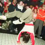 A breakdancer shows off their moves while other dancers watch on from the sidelines.
