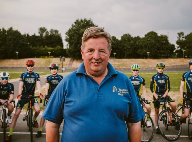 Cycling coach Alan Davies MBE in foreground with members of Maindy Flyers Youth Cycling club stood with bikes behind