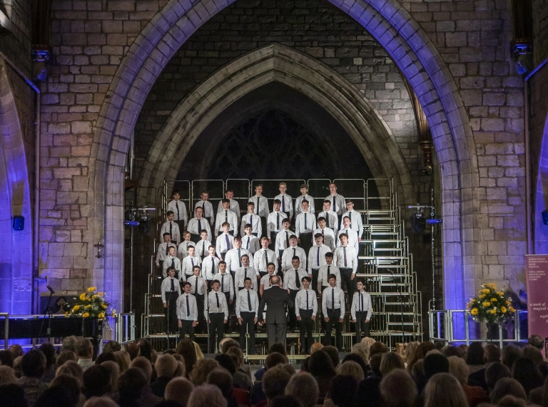 choir of boys under archway singing to audience in cathedral.