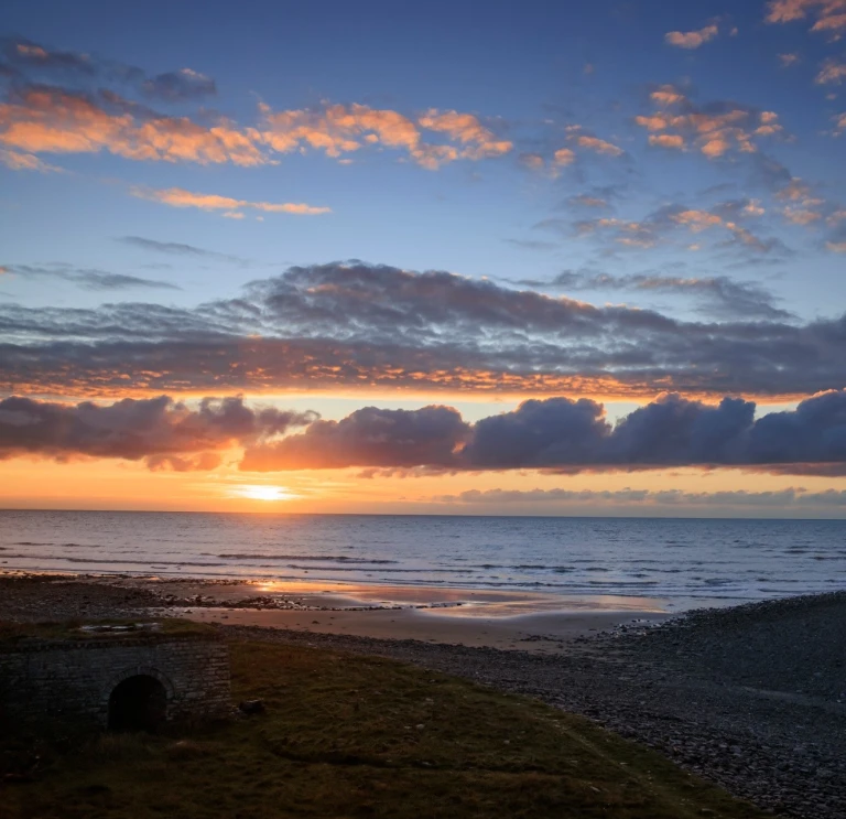 A beautiful and colourful sunset viewed over an expanse of beach and coastline
