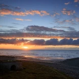 A beautiful and colourful sunset viewed over an expanse of beach and coastline