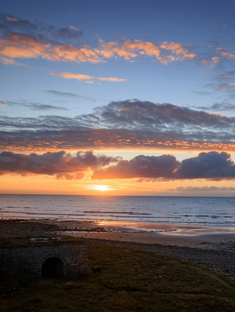A beautiful and colourful sunset viewed over an expanse of beach and coastline