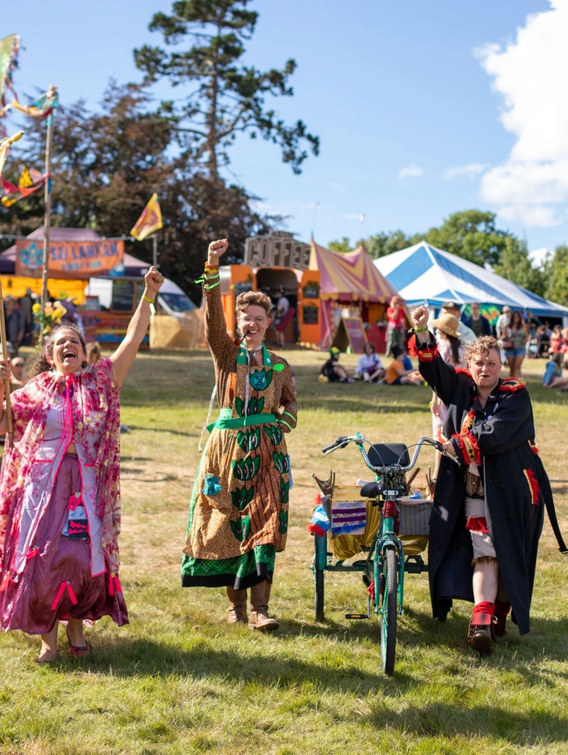 Three people dressed in bright festival costumes raising their arms to wave 