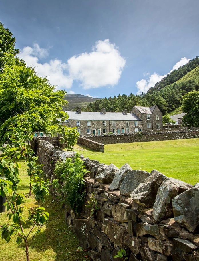 Stone house within green hills and a brick wall in the front.