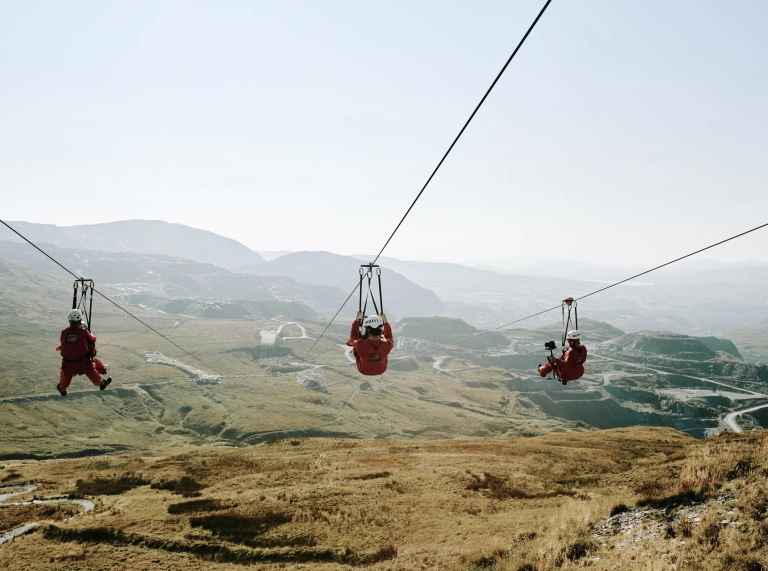 Three people riding a zip-line high above a slate quarry.