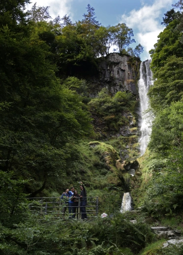People smiling on a bridge at the bottom of the impressive waterfall.