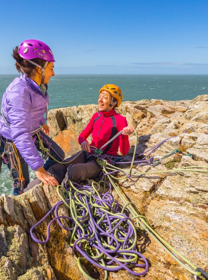 Female rock climber reaching top of sea cliff at Rhoscolyn, Holy Island, Anglesey.
