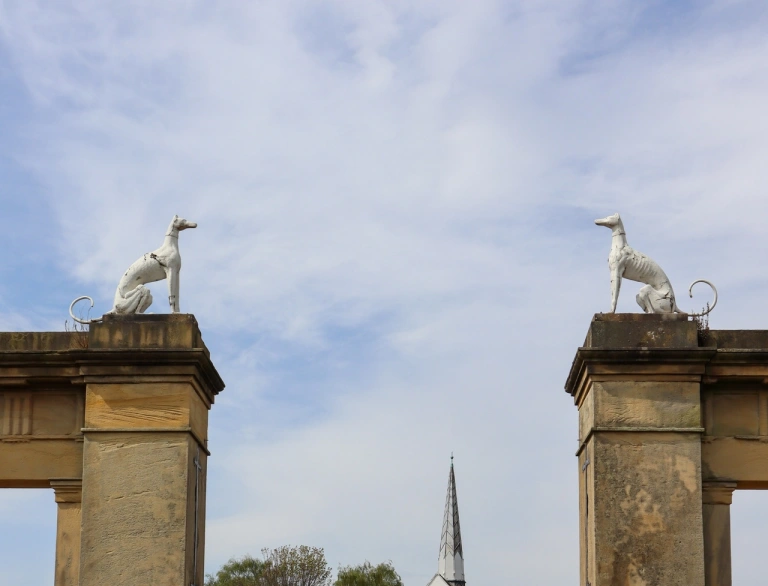 Old stone entrance to a park with carved greyhounds set above two arches