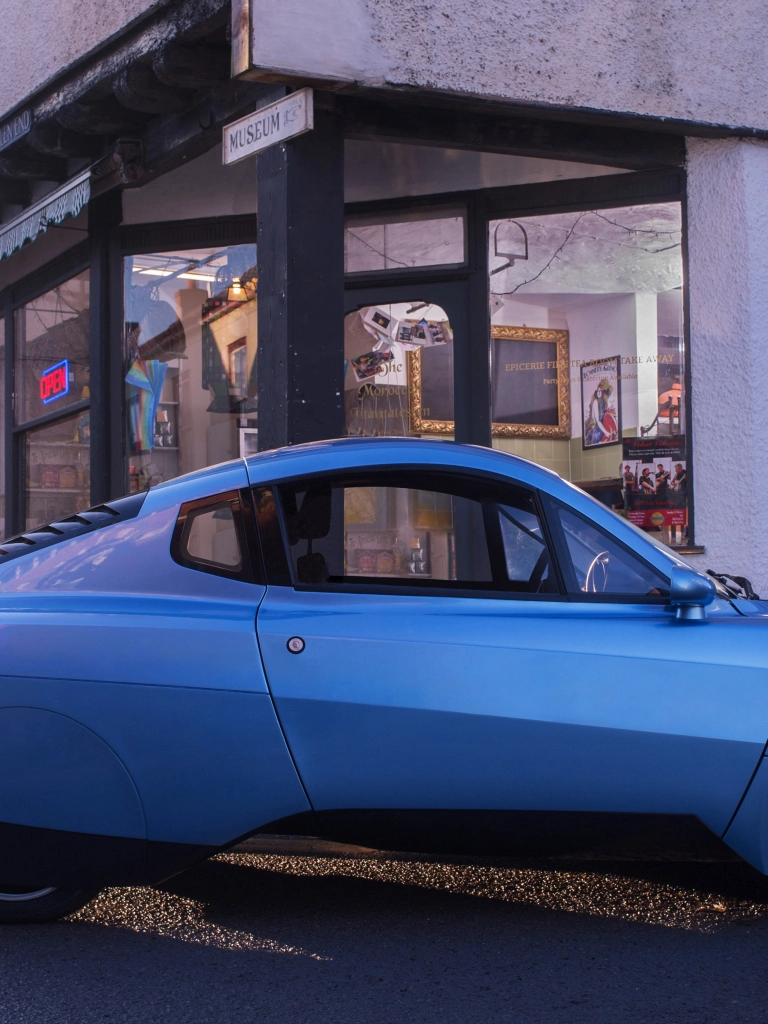 Side view of hydrogen powered car Riversimple Rasa with shop in background