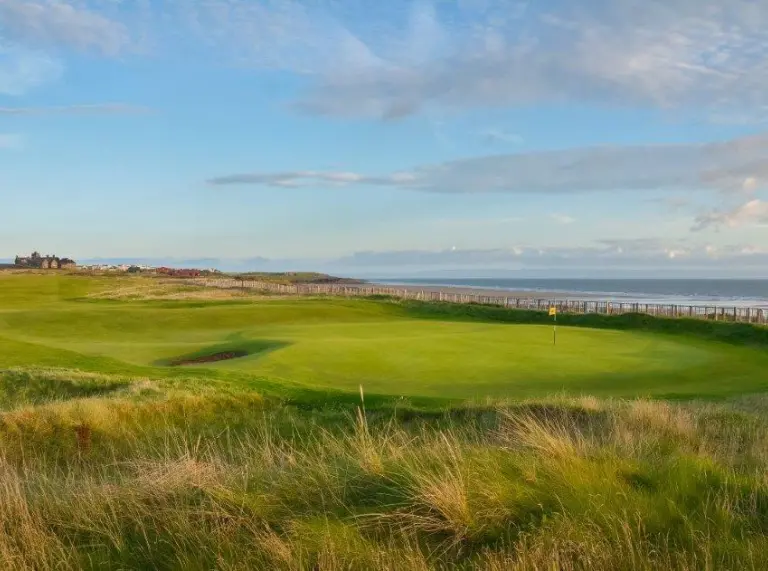 An outdoor scene of a golf green set against a blue sky with the sea in the background 