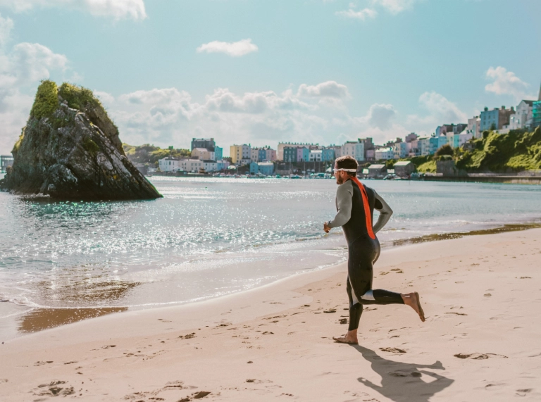 Shane Williams in a wetsuit running into the sea in training for Ironman Wales triathlon on Tenby's North beach.