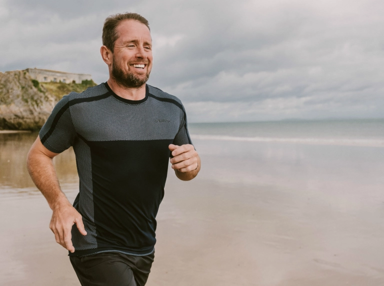 Shane Williams running along  Tenby's North beach in training for Ironman Wales triathlon.