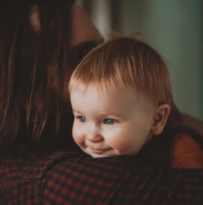 A smiling baby being cuddled by its mother 