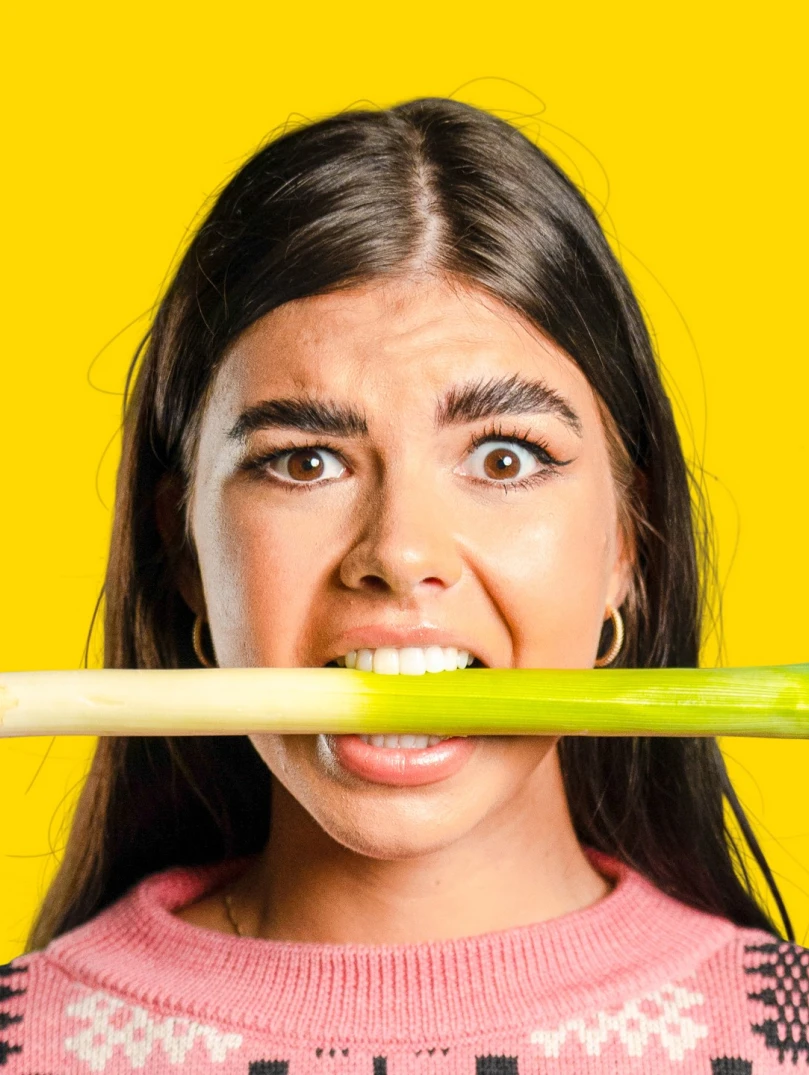 ピンクのジャンパーを着て、口にリーキをくわえた女性