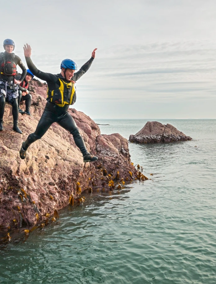 Coasteering group jumping off rocks into sea.