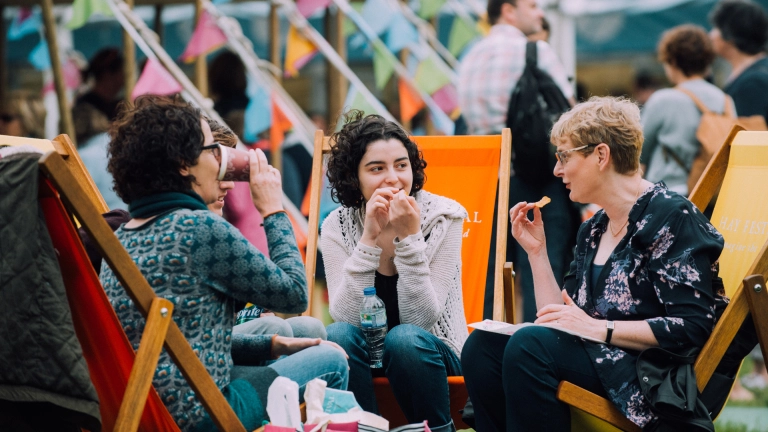 Three women sat on deckchairs eating and drinking.