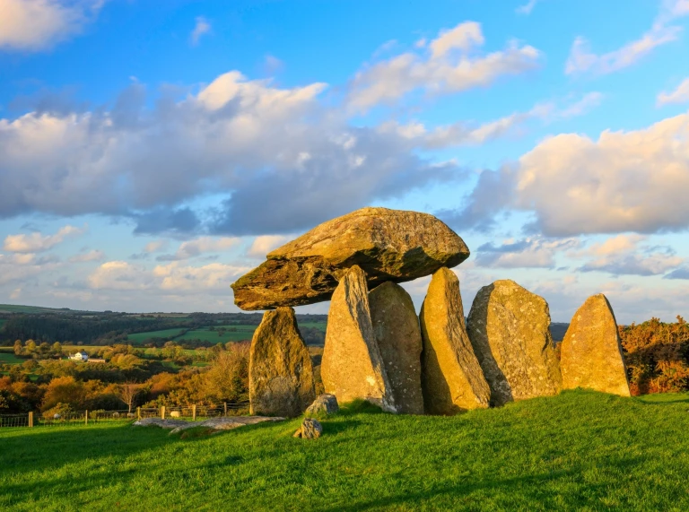 A Neolithic burial chamber in a green field with bright blue sky in the background